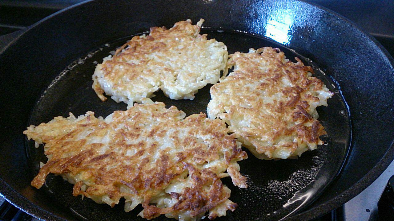 Golden Kartoffelpuffer (German Potato Pancakes) cooking in a black cast iron frypan