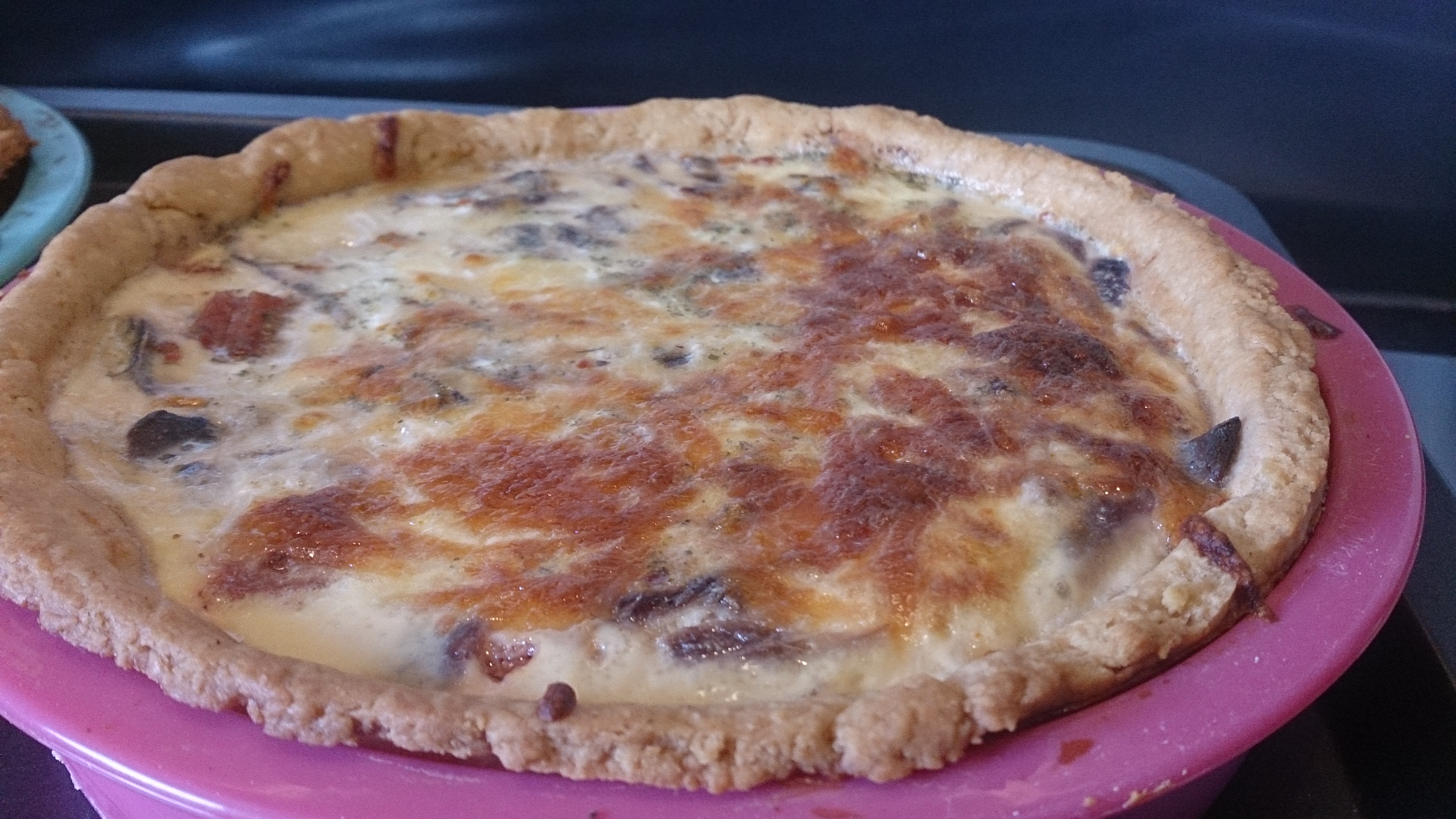 Cooked quiche in a round pink baking tin