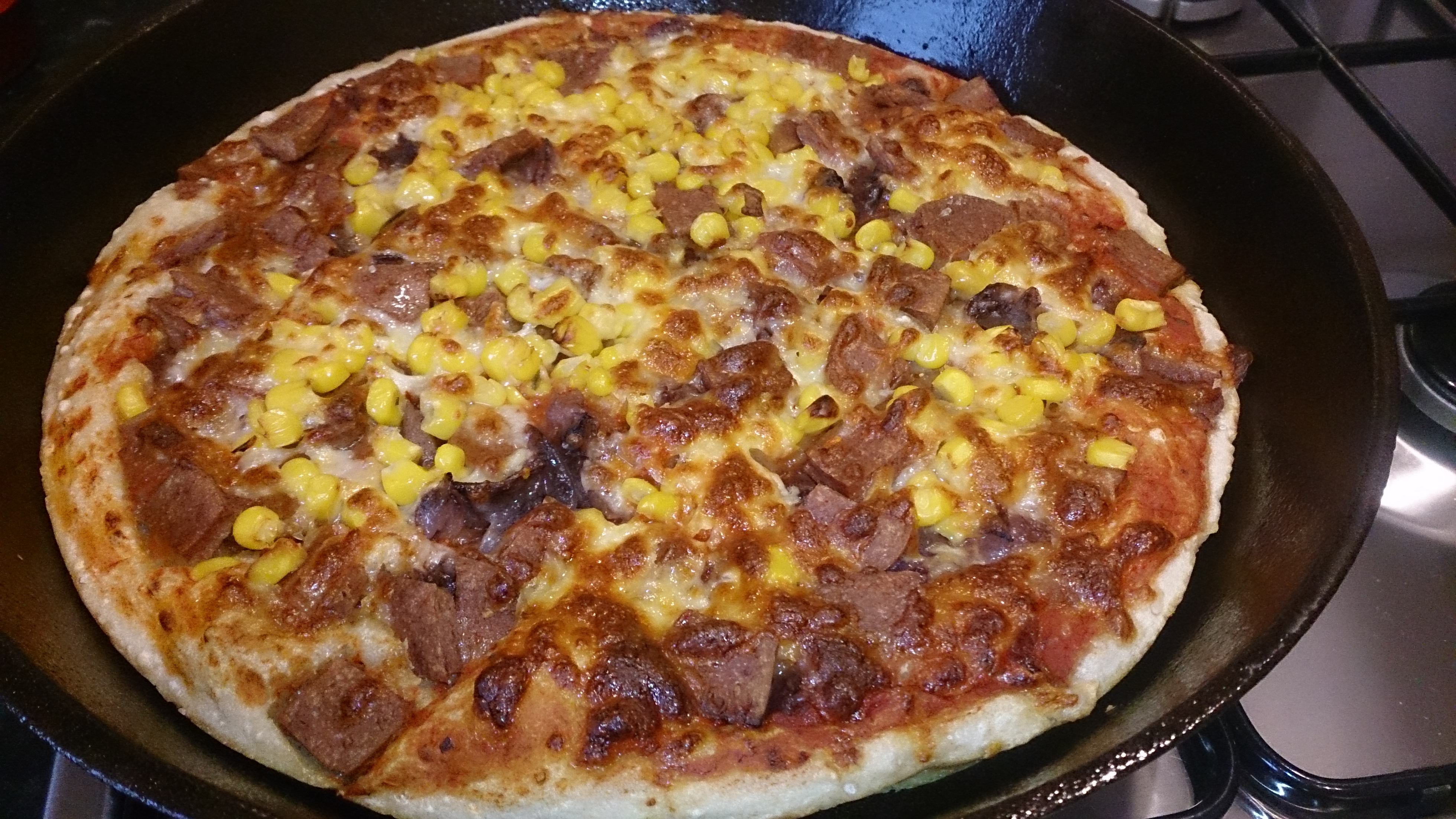 Finished pizza in a cast iron pan topped with sweetcorn