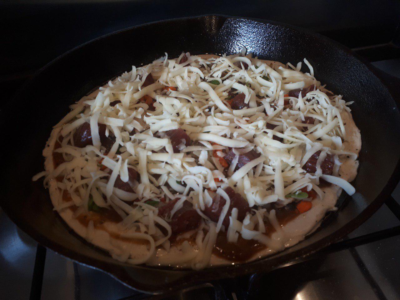 Uncooked pizza in a cast iron pan topped with loads of cheese