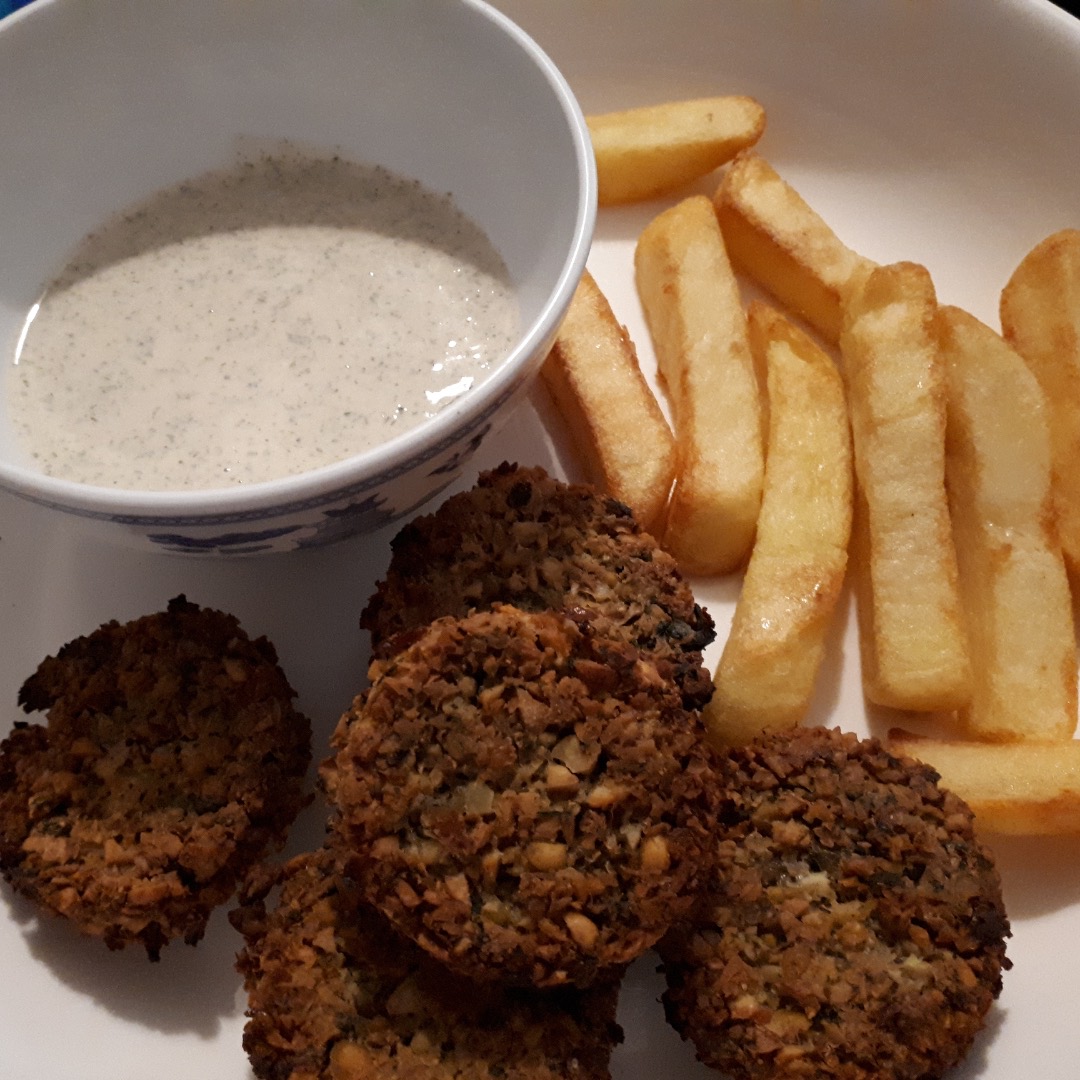 A plate with oven baked falafel, tarator sauce in a small bowl alongside, with french fries