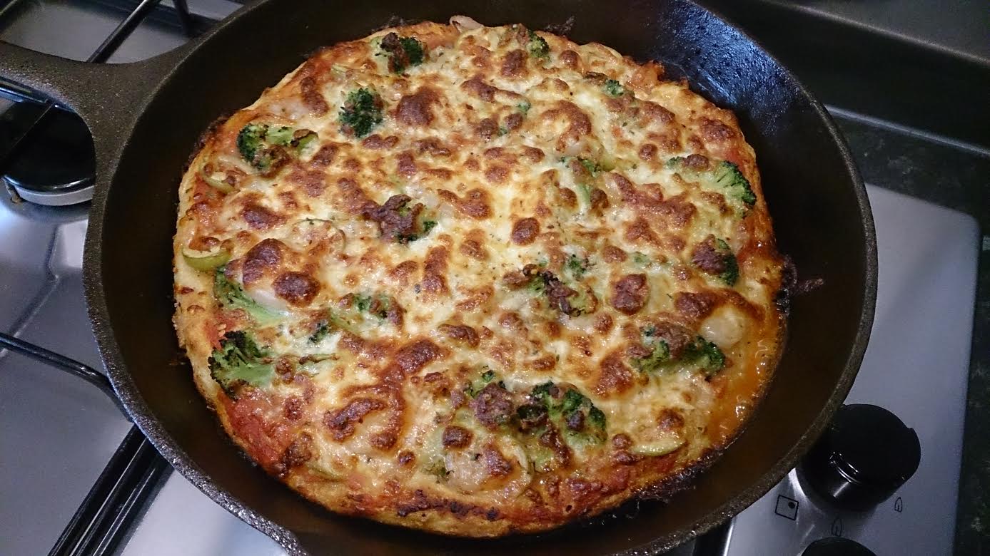 Cooked pizza in a cast iron pan with broccoli and olives