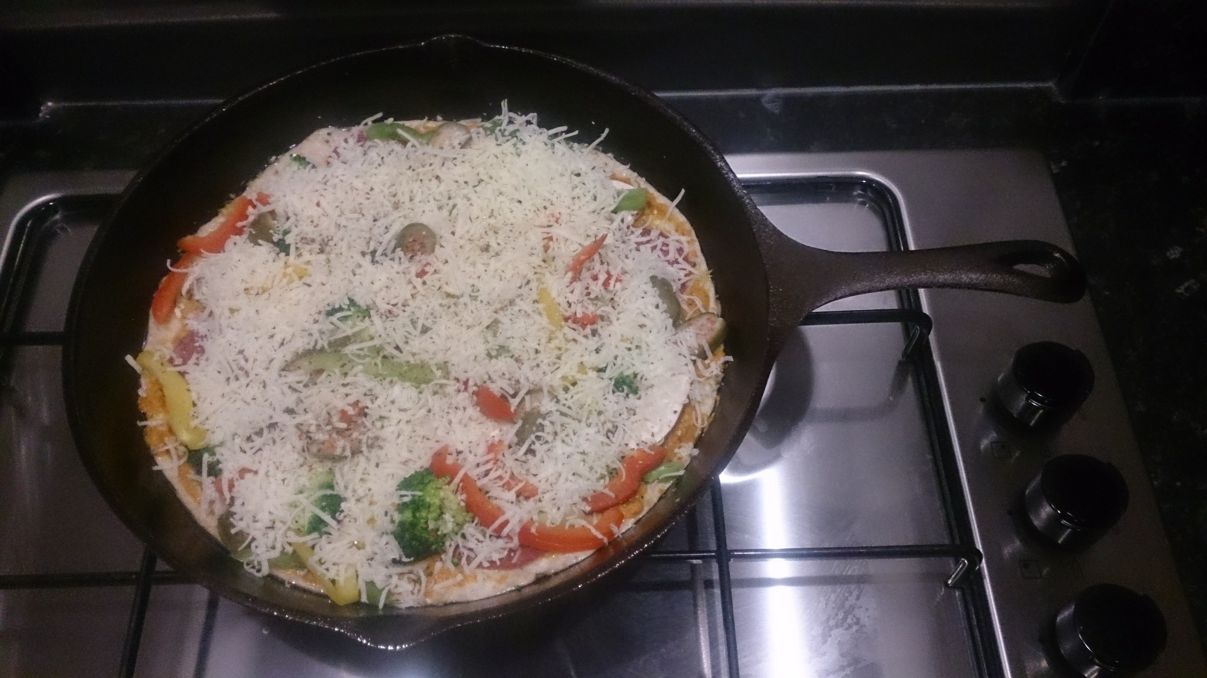 Uncooked pizza in a cast iron pan topped with peppers and cheese